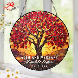 May include: A round stained glass window with a tree design. The tree has red leaves and a brown trunk, set against a yellow and orange background. The text "40TH ANNIVERSARY David & Sophia 04.10.1985" is displayed at the bottom.