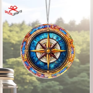 May include: A stained glass style compass ornament with a blue background, gold accents, and a red and gold compass needle. The ornament is hanging from a silver chain.