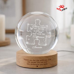 May include: A clear glass sphere resting on a round wooden base. The sphere features an etched puzzle piece design with the text: Never forget you are the piece that made the difference, and the name Amanda. The base has engraved text.