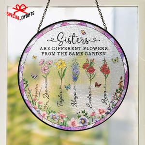 May include: Round stained glass art piece with a black metal frame and chain for hanging. The artwork features the text "Sisters are different flowers from the same garden" and names below colorful flower illustrations.