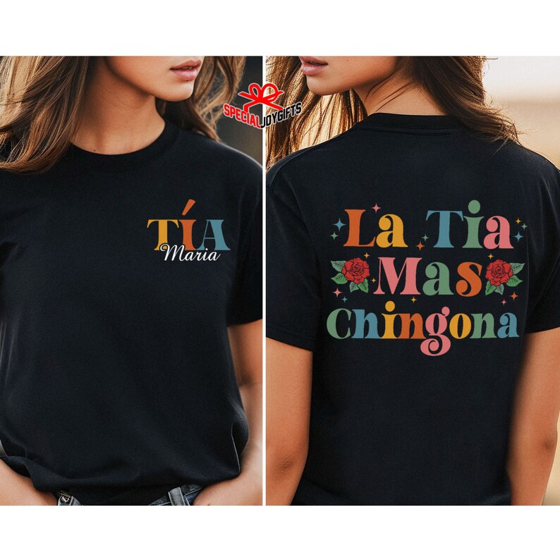以下が含まれることがあります： 黒のTシャツで、背面には「La Tia Mas Chingona」というカラフルなグラフィックが描かれており、花と星が描かれています。Tシャツの前面には「Tia Maria」というカラフルなグラフィックが描かれています。