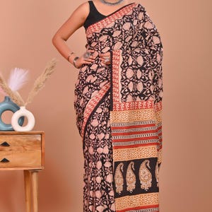 May include: A black and red floral print saree with a decorative border. The saree features a black base with a repeating floral pattern in a lighter color. The border has a red and gold design. The saree is draped on a person.