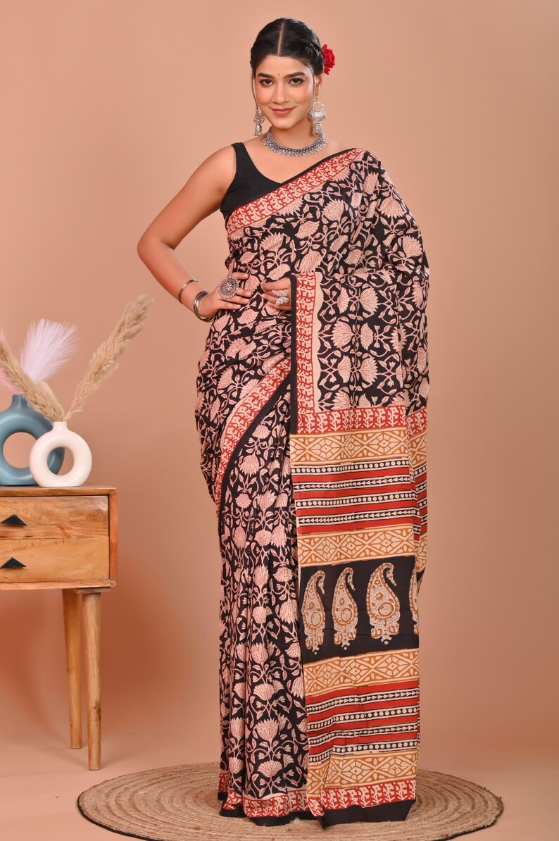 May include: A black and red floral print saree with a decorative border. The saree features a black base with a repeating floral pattern in a lighter color. The border has a red and gold design. The saree is draped on a person.