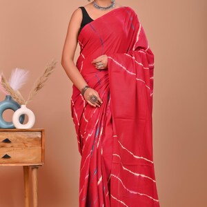 May include: A vibrant red saree with white and blue striped patterns. The traditional Indian garment is draped over a person, showcasing the intricate design and flowing fabric. The saree is a bold statement piece.