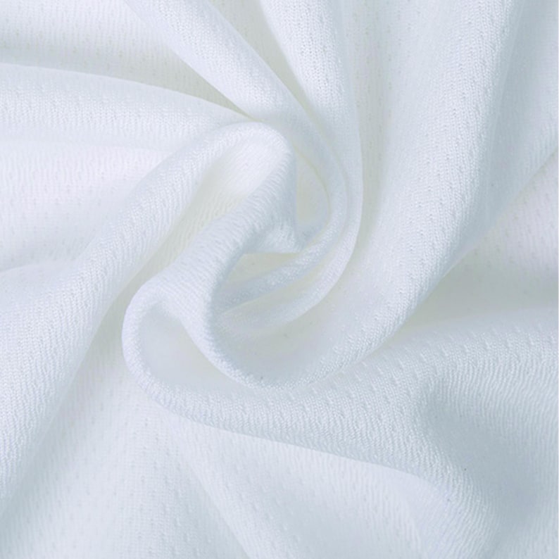 May include: Close-up of white fabric with a textured, slightly raised dot pattern. The fabric is draped in soft folds, creating shadows and highlights. The material appears lightweight and breathable, suitable for clothing.