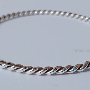 Könnte beinhalten: Ein silbernes Armreif-Armband mit einem gedrehten Seil-Design. Das Armband ist schlicht und elegant.