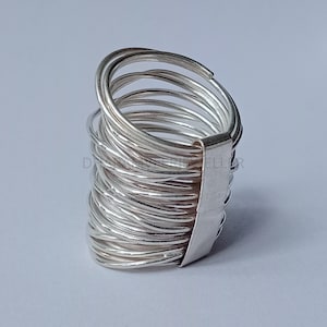 May include: A silver ring made of multiple thin bands stacked on top of each other. The bands are all connected to a flat silver band that forms the base of the ring.