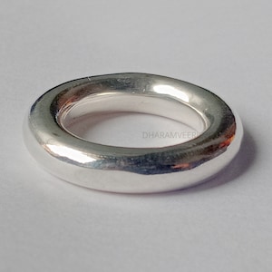 Puede incluir: Un anillo de plata liso con una banda ancha y redondeada. El anillo está hecho de metal pulido y tiene un diseño simple y moderno.