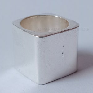 May include: A silver square ring with a smooth, polished finish. The ring is thick and has a wide band.