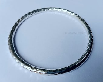May include: A silver bangle bracelet with a hammered texture. The bracelet is round and has a smooth, polished finish.
