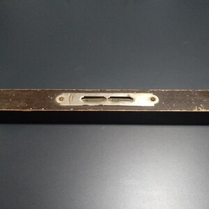 May include: A vintage wooden spirit level, finished in dark brown, with a metal plate featuring two viewing windows. The level shows signs of wear, with chipped paint and a distressed look. A classic tool for carpentry and construction.