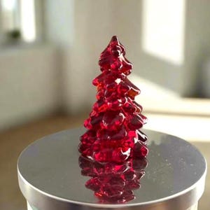 以下が含まれることがあります： 銀色のキャンドルジャーの蓋の上に、赤いガラス製のクリスマスツリーのオーナメントが置かれています。ジャーには「ハンティントン」と書かれたラベルが付いています