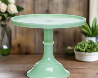 May include: A light green glass cake stand with a round base and a wide, flat top. The stand is made of a smooth, glossy material.