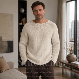 Könnte beinhalten: Ein cremefarbener, langärmeliger Grobstrickpullover mit Rundhalsausschnitt und Raglanärmeln. Das Kleidungsstück zeichnet sich durch eine dicke, strukturierte Garnkonstruktion mit einem sichtbaren Maschenbild aus und wird über einer dunkelbraunen Hose getragen.