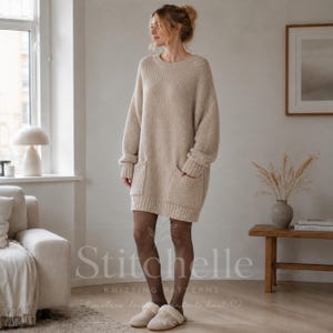 May include: A beige long-sleeved sweater dress featuring a ribbed knit texture, a round neckline, and two large front patch pockets. The garment has a relaxed fit with dropped shoulders and ribbed cuffs, extending to mid-thigh length.