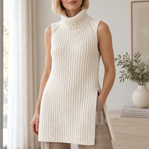 Peut inclure: Un gilet sans manches de couleur crème avec une texture en tricot côtelé épais, un col roulé montant et des fentes latérales profondes partant de l'ourlet. Le vêtement présente une silhouette droite et un motif à côtes verticales.