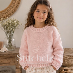 Könnte beinhalten: Ein hellrosa langärmeliger Strickpullover mit geripptem Rundhalsausschnitt und gerippten Bündchen. Der Pullover zeigt ein zentrales weißes Grafiklogo mit dem Schriftzug Stitchelle, einer kleinen Blattillustration darüber und einem Herz.