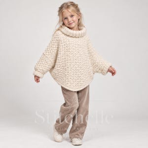 May include: An off-white, chunky knit poncho featuring a high, ribbed turtleneck collar and long sleeves with ribbed cuffs. The garment has a textured, repeating stitch pattern and a rounded hemline, paired with light brown, straight-leg trousers.