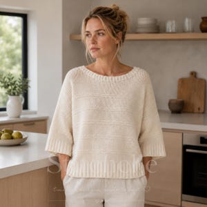 May include: An off-white, cream-coloured knit jumper featuring a wide boat neckline, three-quarter length sleeves, and a ribbed hem. The garment displays a horizontal striped texture created by alternating knit patterns across the torso and sleeves.