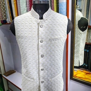 May include: A white sleeveless vest with a textured pattern and button closures. The vest has a mandarin collar and a pocket on the left side.