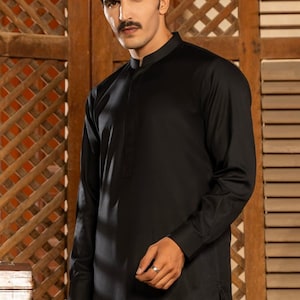 May include: A black long-sleeved shirt with a mandarin collar. The shirt has a single button closure at the neck and a side slit on the bottom.