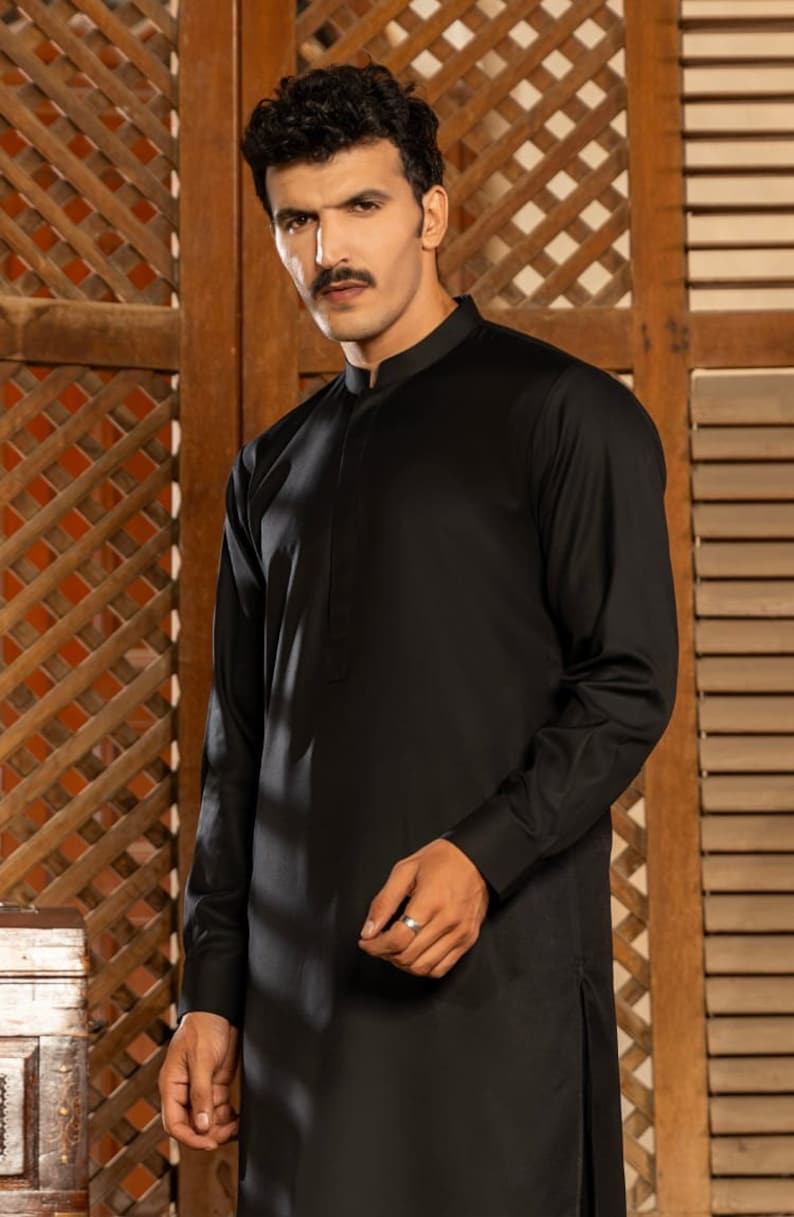 May include: A black long-sleeved shirt with a mandarin collar. The shirt has a single button closure at the neck and a side slit on the bottom.