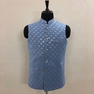May include: A light blue sleeveless vest with a diamond pattern and silver embellishments. The vest has a mandarin collar and button closure.
