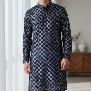 May include: Navy blue long tunic with a mandarin collar and silver circular pattern. The tunic is paired with white pants. The outfit is suitable for formal occasions.