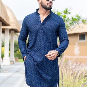 May include: A navy blue long-sleeved kurta with a geometric pattern. The kurta has a mandarin collar and a button closure. The model is wearing white pants.