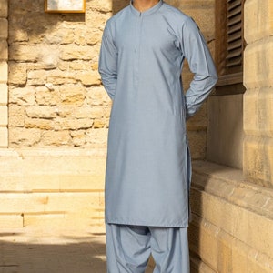 May include: A light blue long-sleeved shirt with a mandarin collar and a button closure. The shirt is worn with matching light blue trousers. The person is wearing sunglasses.