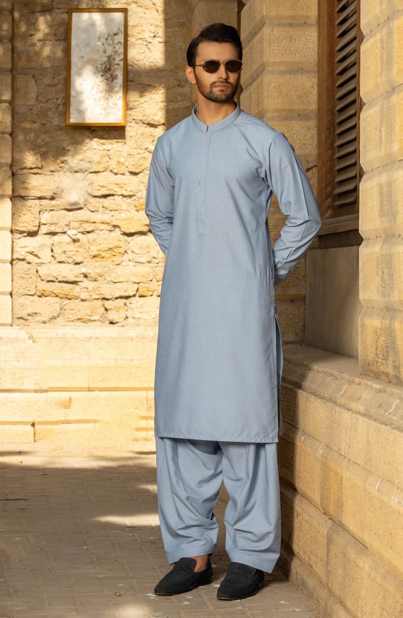 May include: A light blue long-sleeved shirt with a mandarin collar and a button closure. The shirt is worn with matching light blue trousers. The person is wearing sunglasses.