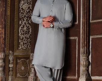 May include: A light blue long-sleeved shirt with a button-up collar and matching pants. The person is standing in front of a wooden door with intricate carvings.