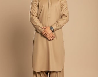 Op de afbeelding: Een bruin trouw kurta-pak. Het overhemd met lange mouwen heeft een opstaande kraag en een knoopsluiting. De bijpassende broek heeft een losse pasvorm. De outfit wordt gecombineerd met bruine geklede schoenen. De tekst "WEDDING KURTA" staat onderaan.