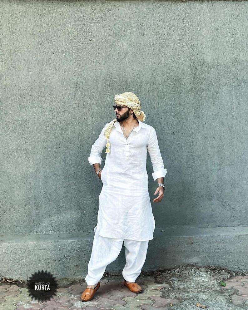 May include: A white long-sleeved kurta with a button-up collar and a matching white shalwar. The man is wearing a gold turban and sunglasses. The text "Wedding Kurta" is visible in the lower left corner of the image.