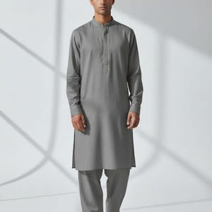 May include: A gray kurta suit with a mandarin collar, long sleeves, and matching pants. The outfit is worn with white sneakers. The text "WEDDING KURTA" is printed at the bottom left of the image.