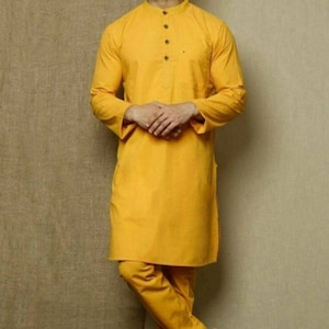 May include: A yellow long-sleeved kurta with a button-up collar and matching pants. The man is wearing brown sandals.