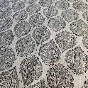 May include: White and black patterned quilt featuring a repeating leaf design. The leaves are detailed with intricate lines and shapes, creating a textured appearance. The quilt is stitched with a dotted pattern, adding to its handmade aesthetic.