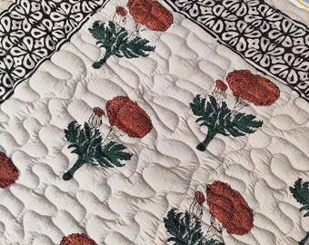 May include: Cream-colored quilted fabric with a repeating pattern of rust-colored flowers and green leaves. The border features a dark brown and white geometric design. The fabric has a soft, textured appearance.