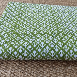 May include: Folded fabric featuring a repeating white and green floral pattern. The fabric is a light green colour with a white floral design. The fabric is folded and appears to be made of cotton or a similar material.