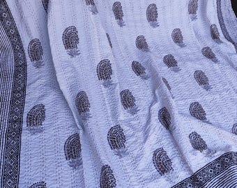 May include: White and gray floral patterned quilt. The quilt features a repeating design of gray floral motifs on a white background. The edges are bordered with a black and white geometric pattern. The quilt is made of a soft, textured fabric.