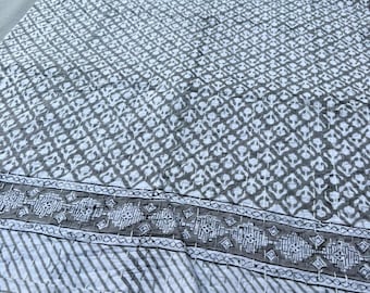 Puede incluir: Un edredón plegado con estampado blanco y gris. El edredón presenta un diseño geométrico repetitivo en gris y blanco. Se ve un borde decorativo con formas geométricas y líneas diagonales.