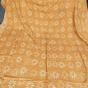 May include: Mustard yellow quilt with white floral patterns. The quilt features a repeating design of stylized flowers and a decorative border. The stitching is visible, adding texture to the fabric. This handmade quilt is perfect for adding a touch of warmth and style to any bedroom.