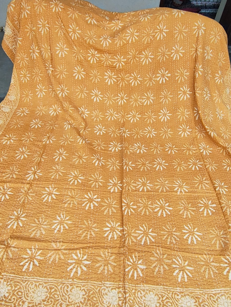 May include: Mustard yellow quilt with white floral patterns. The quilt features a repeating design of stylized flowers and a decorative border. The stitching is visible, adding texture to the fabric. This handmade quilt is perfect for adding a touch of warmth and style to any bedroom.