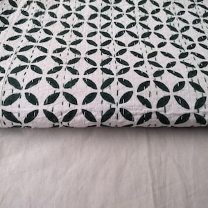 May include: White and dark green patterned quilt. The quilt features a repeating floral design with dark green leaf-like shapes on a white background. The quilt is folded, showing the pattern and texture of the fabric.