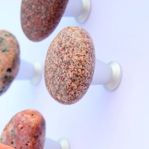 Könnte beinhalten: Ein Satz von acht einzigartigen, natürlichen Stein-Knöpfen in Rosatönen, Rot und Braun. Jeder Knopf ist auf einer silbernen Metallbasis montiert und bereit, an einem Schrank oder einer Schublade angebracht zu werden.