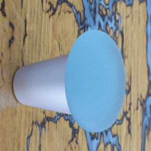 以下が含まれることがあります： 丸いすりガラスのトップを持つ銀色と薄い青色のノブ。ノブは青と茶色のマーブル模様の木製面に設置されています。