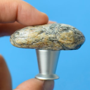May include: A natural stone cabinet knob with a silver base. The stone is a light brown with dark grey and black streaks.