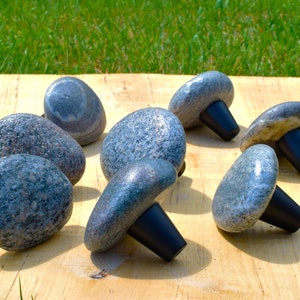 Könnte beinhalten: Ein Satz von acht grauen Steingriffmuscheln mit schwarzen Metallsockeln. Die Griffe sind pilzförmig und haben ein natürliches, rustikales Aussehen.