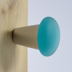 May include: A light blue glass knob with a silver metal base mounted on a wooden surface.