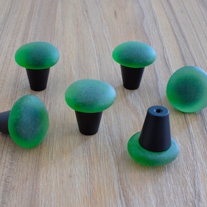 Può includere: Sei pomelli per armadi in vetro verde con basi nere. I pomelli hanno la forma di un fungo con una parte superiore arrotondata e uno stelo.